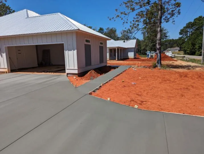 New concrete driveway leading to a white garage over red clay