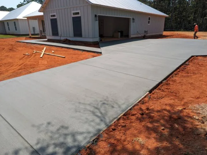 Wide view of the new concrete driveway at the white garage with red clay around the pour